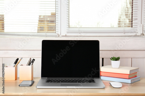 Comfortable workplace with modern laptop and blinds on window