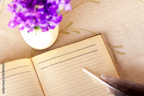 Bird feather on old notebook and blue flowers in vase