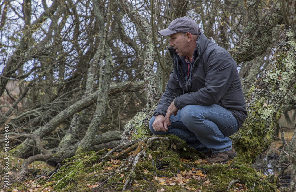 man in copse crouching looking at scenery