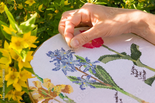 Female hand embroider flowers. Young girl embroiders a white material.