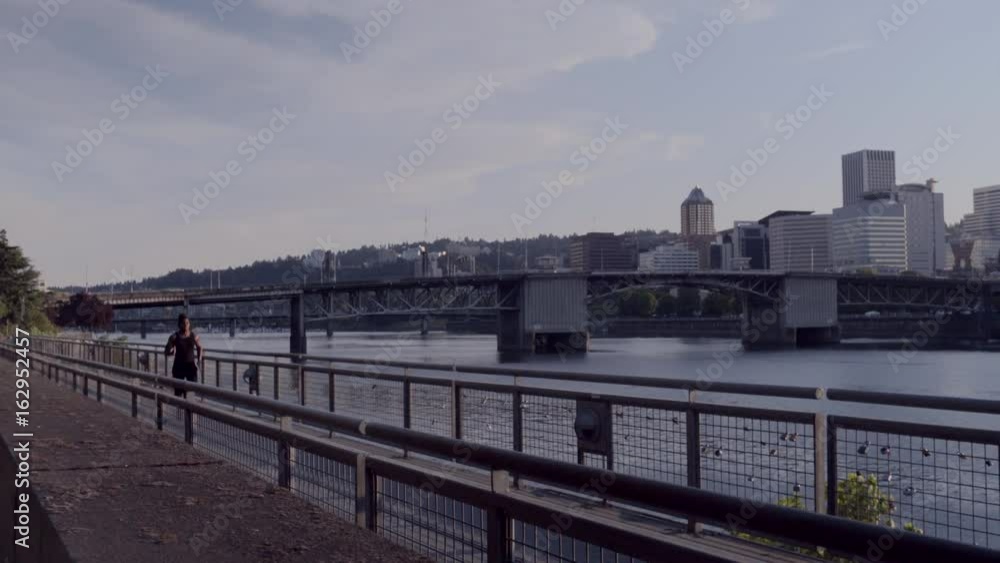 Man Runs Along Waterfront, City Skyline In Background Man Runs Along Waterfront, City Skyline In Background