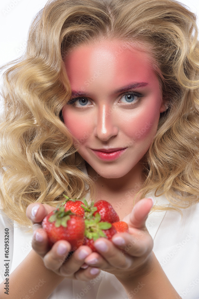 Beautiful blonde woman face with pink makeup. Glamour fashion model portrait with strawberry. Colorful pigment on the face, glossy skin, bright make-up. White backdrop Beautiful blonde woman face with pink makeup. Glamour fashion model portrait with strawberry. Colorful pigment on the face, glossy skin, bright make-up. White backdrop