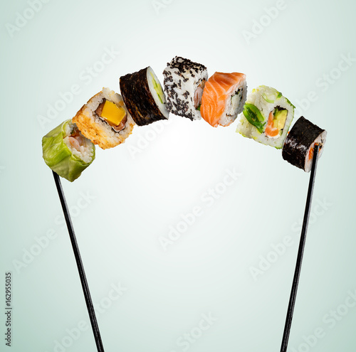 Sushi pieces placed between chopsticks on soft background