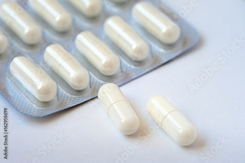 Two white pills lie on a white table. Packing tablets in the background. Concept of health, medicine, pharmacology