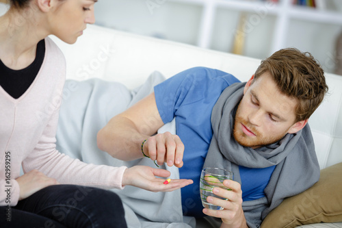 loving wife taking care of sick husband lying on sofa