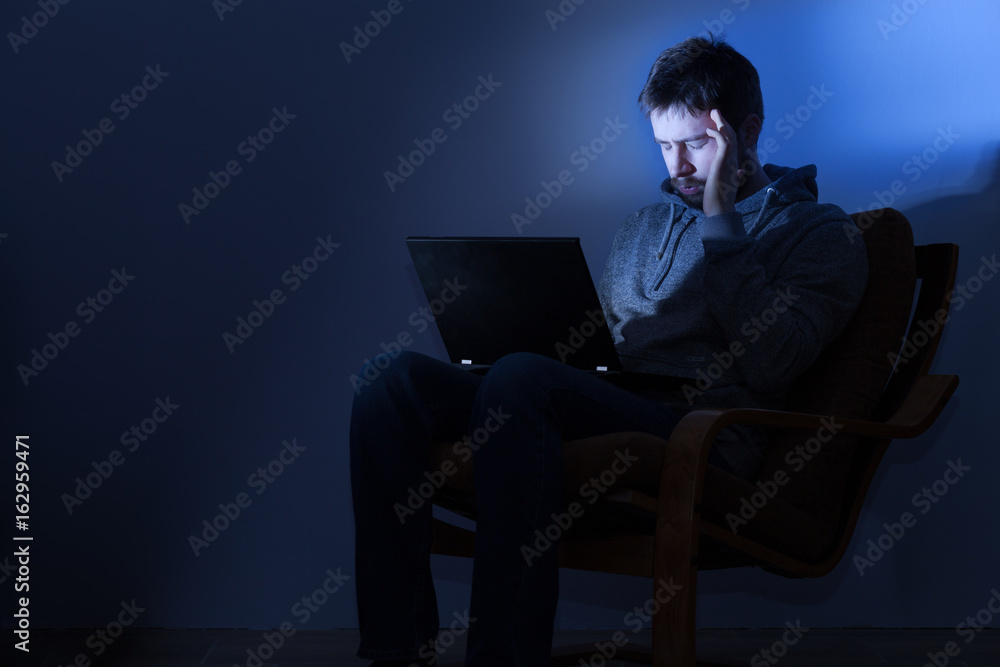 Weary man with a strong headache and closed tired aching eyes working on a laptop in a dark room at night Weary man with a strong headache and closed tired aching eyes working on a laptop in a dark room at night