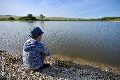 The boy is sitting by the river and wants to fish