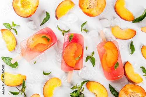 Fototapeta Naklejka Na Ścianę i Meble -  Summer desserts. Frozen drinks. Sweet fruit popsicles from frozen peach tea with mint. On a white marble table, with ingredients - peaches, mint, ice. Copy space top view