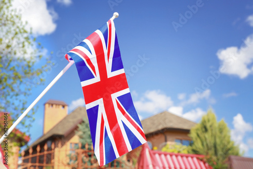 Waving flag of United Kingdom and house roof on blue sky background