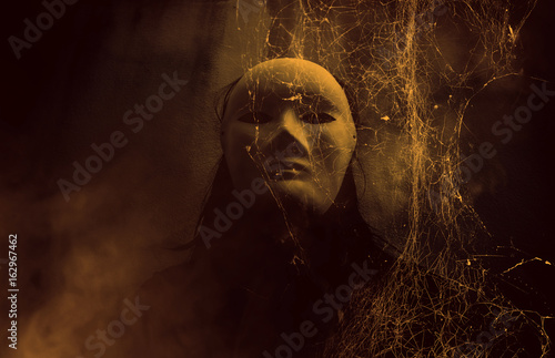 Mysterious woman in black wearing white mask hidden behind spider web,Scary background for book cover