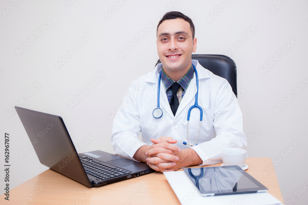 confident male doctor sitting at office desk and smiling, medical healthcare concept.