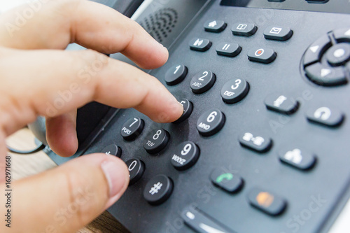 Fotografi Closeup of male hand holding telephone receiver while dialing a telephone number to make a call using a black landline phone