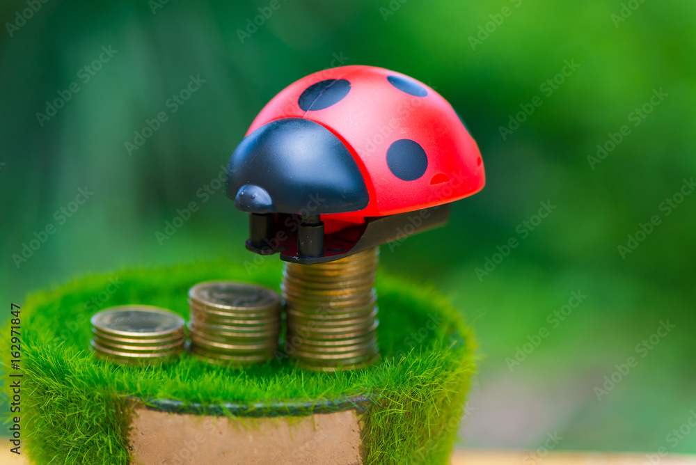 Fototapeta premium Stack of gold coin on artificial grass in pot, on wooden table with green nature background.