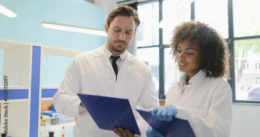 Mix Race Scientists Discuss Results Of Research Experiment Holding Documents In Modern Laboratory Talking Slow Motion 60