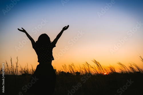 silhouette of woman open arms under the sunset