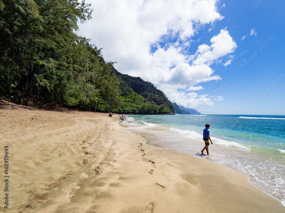 10 year old boy walking over golden sand on sunny Ke'e Beach, Kauai, Hawaii