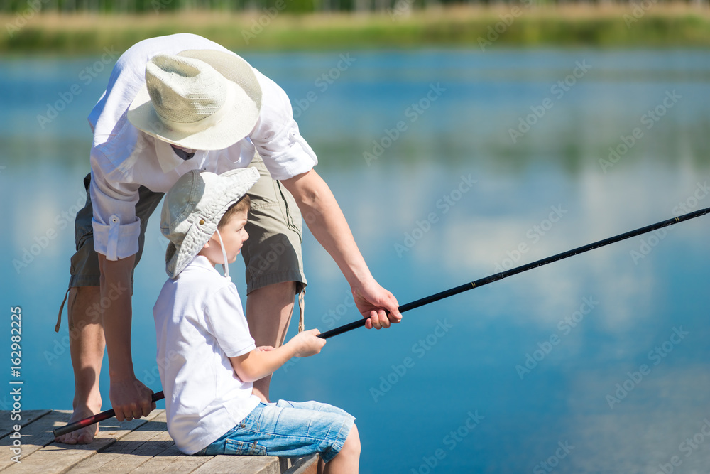 Dad helps his son catch fish with a fishing rod on the river Dad helps his son catch fish with a fishing rod on the river