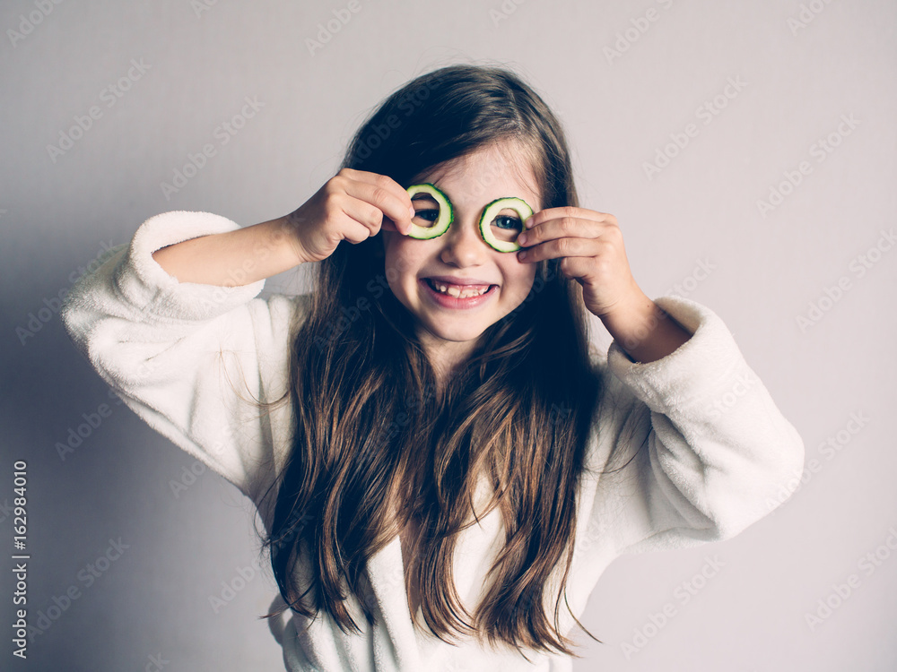 Little girl with cucumbers on her face, concept of beauty and health