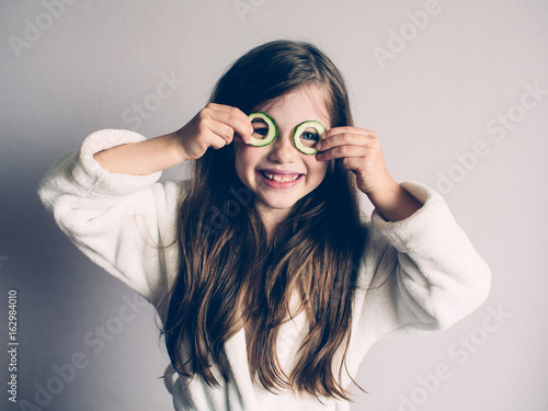 Obraz na płótnie Little girl with cucumbers on her face, concept of beauty and health w salonie