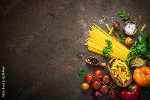 Italian food background. Uncooked Pasta spaghetti tomatoes herbs.