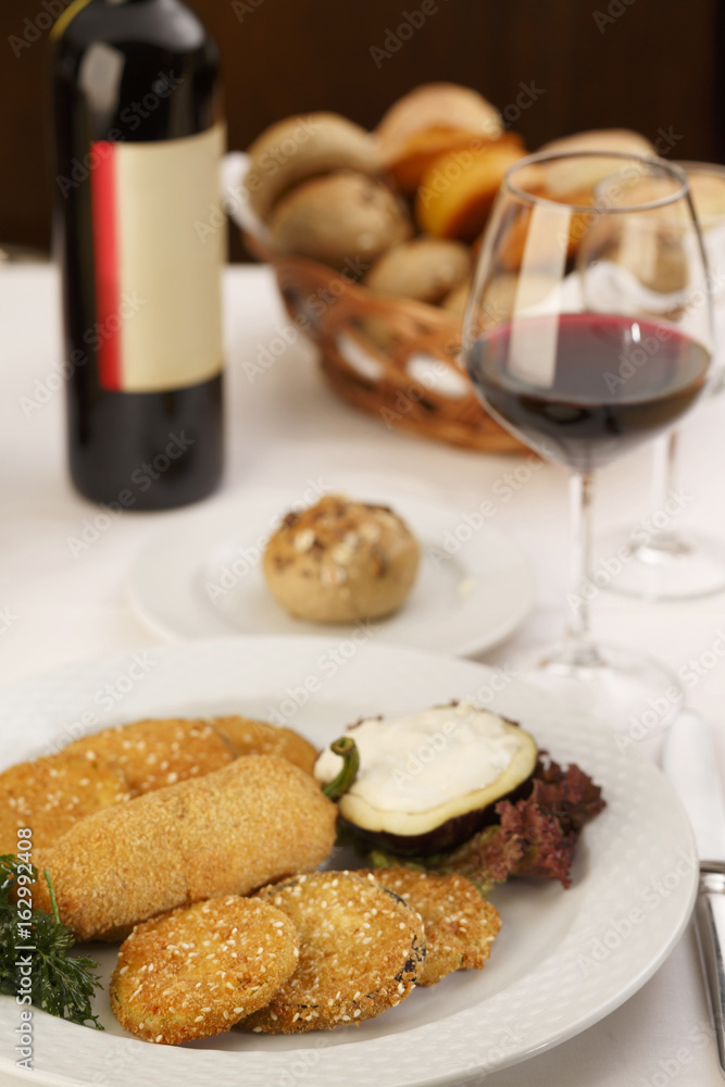 Breaded and fried red bell pepper and eggplant arranged on a plate, Wine bottle and wineglass in background, Traditional dish in elegant setting, Selective focus with soft light Breaded and fried red bell pepper and eggplant arranged on a plate, Wine bottle and wineglass in background, Traditional dish in elegant setting, Selective focus with soft light