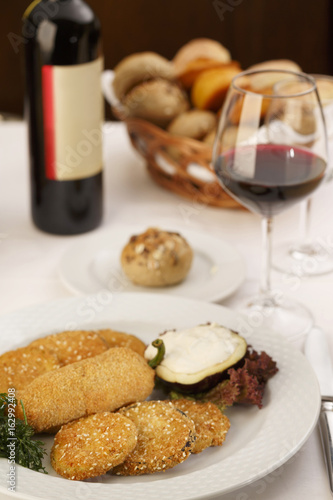 Breaded and fried red bell pepper and eggplant arranged on a plate, Wine bottle and wineglass in background, Traditional dish in elegant setting, Selective focus with soft light