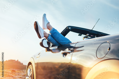 Tableau sur toile A young woman rests and pushes her sneakers out of the convertible to enjoy the