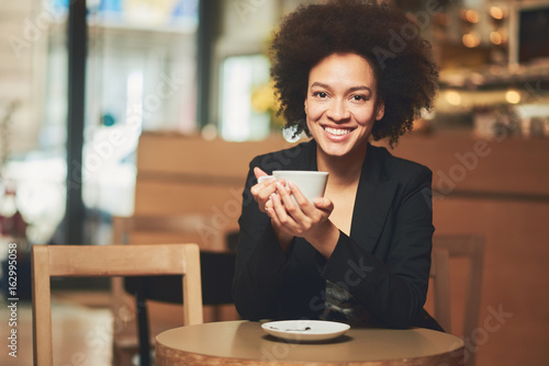 Mixed race business woman taking pause from work and sitting in coffee shop while drinking coffee