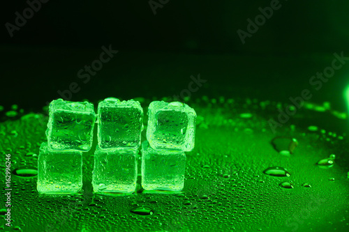 Water drop with ice cubes on lighting green background.