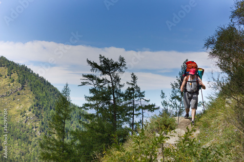 A man with a backpack and trekking sticks walks along the mountain trail