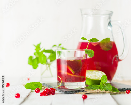 Compote in a glass jug and a glass. Berries and lime  red and green. Fresh mint leaves. Copy space.