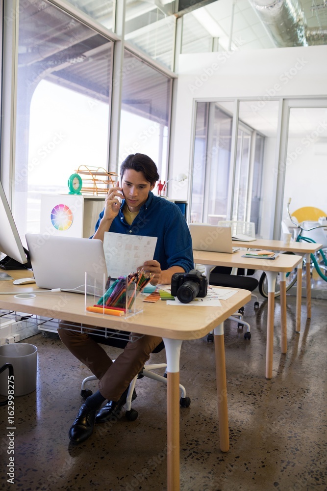 Male executive talking on mobile phone while working at his desk Male executive talking on mobile phone while working at his desk