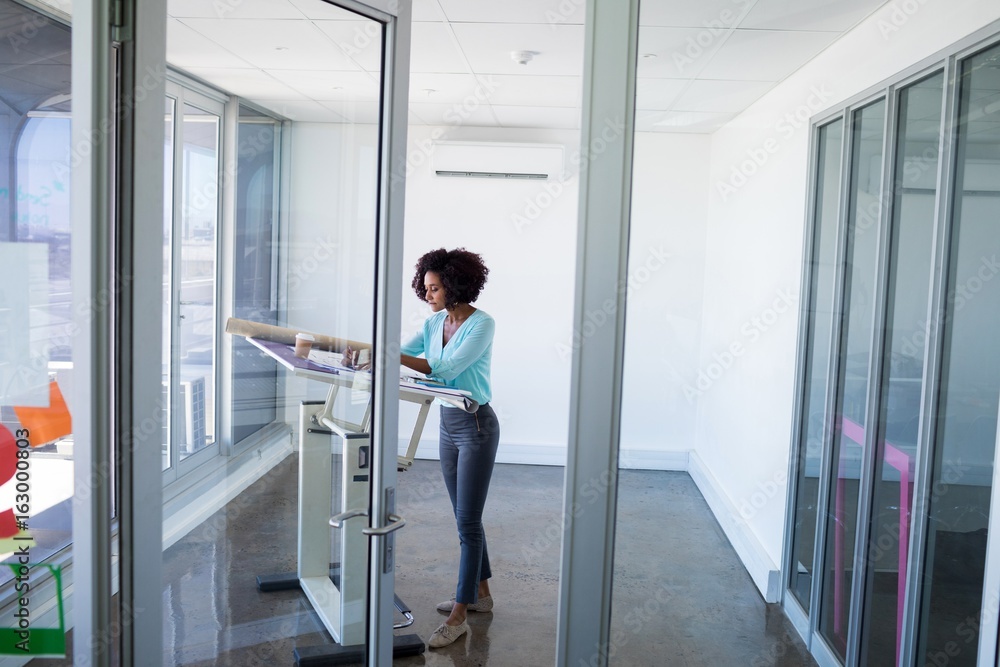 Female architect working on blueprint over drafting table Female architect working on blueprint over drafting table