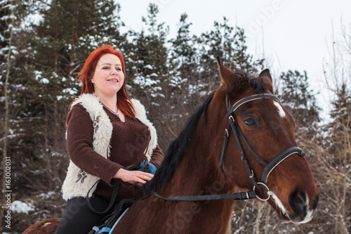 Woman with red hair and big horse outdoor in winter