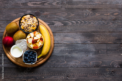 Healthy breakfast, cereal with yogurt, strawberries, blueberry, apple, banana, on rustic wooden.  Top view