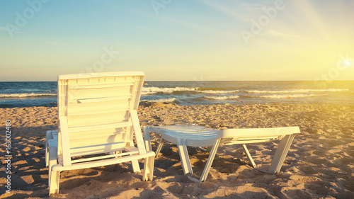 Two deckchairs on the beach with bright sun and waves