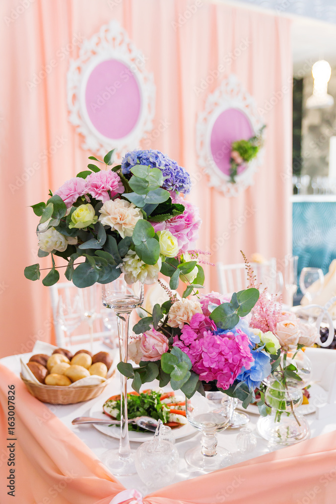 Table set for wedding banquet with floral composition of roses and hydrangea. Flower decoration in tall vase.