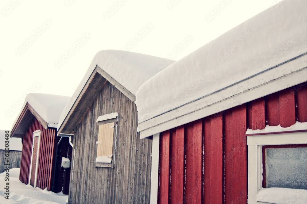 Three small houses/cabins standing close together in winter with lots of snow on the roof tops.