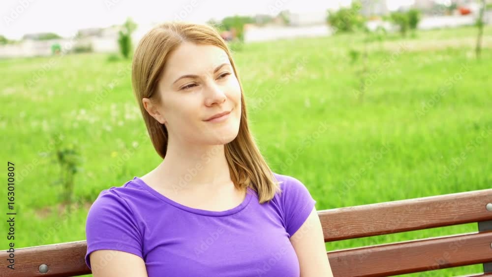 Slow Motion Happy Smiling Young Woman Enjoying Nature. Sitting on bench in green park. Freedom loneliness concept Slow Motion Happy Smiling Young Woman Enjoying Nature. Sitting on bench in green park. Freedom loneliness concept