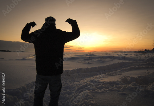 Silhouette of a man standing in a snowy and winter landscape. Sunset and winter field.