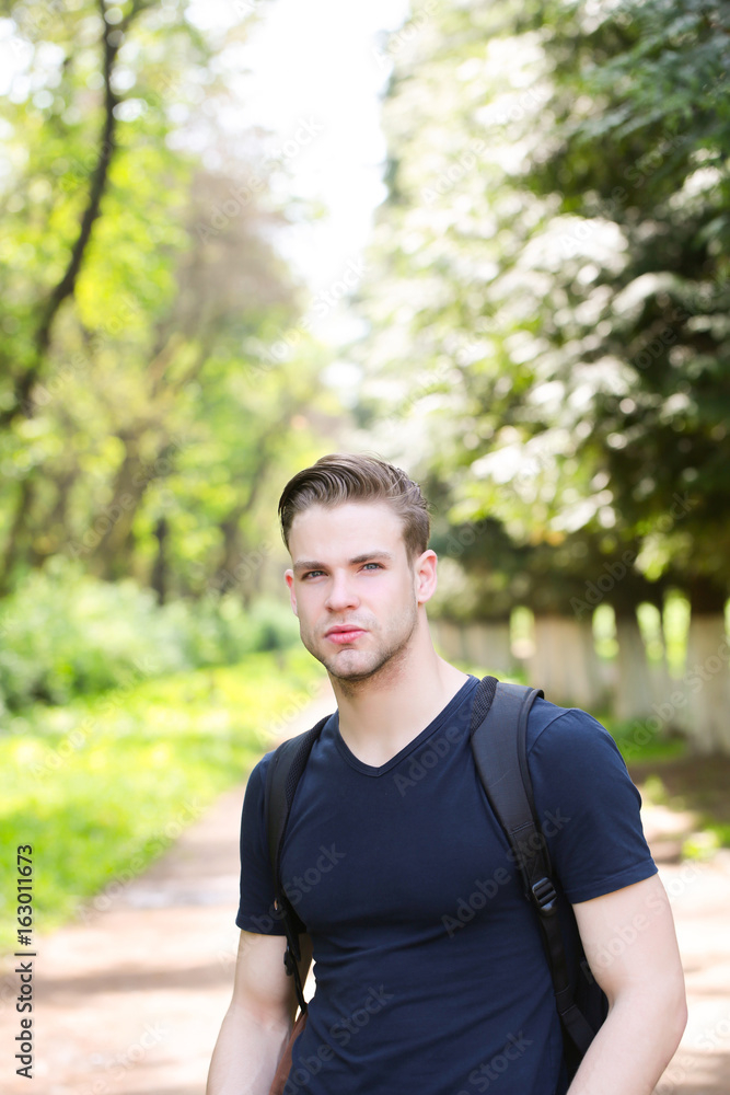 Man with stylish hairdo, sportive outfit, black backpack in park