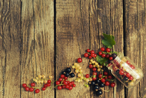 Black, red and white currant berries in glassware on a wooden background.