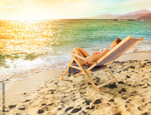 Fototapeta Naklejka Na Ścianę i Meble -  Girl tans on a deck chair on a beautiful beach