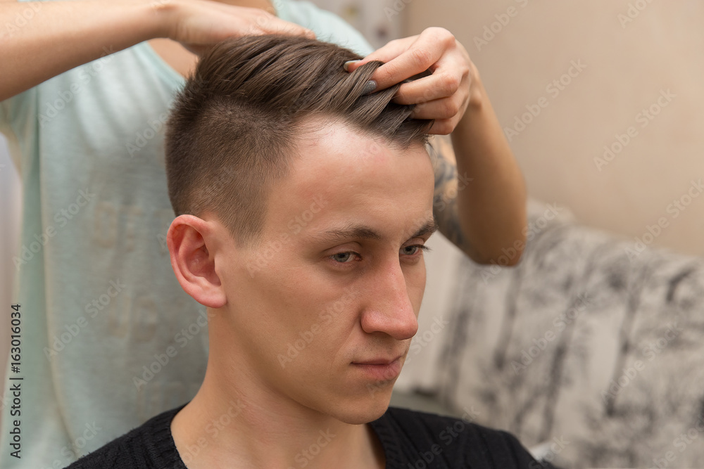 The hands of young barber making haircut to attractive man in barbershop The hands of young barber making haircut to attractive man in barbershop