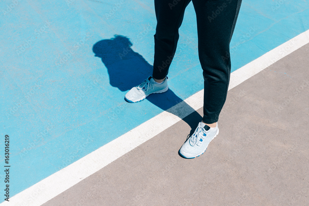 Ταπετσαρία Cropped image of female legs in sneakers and black pants standing on a blue spor