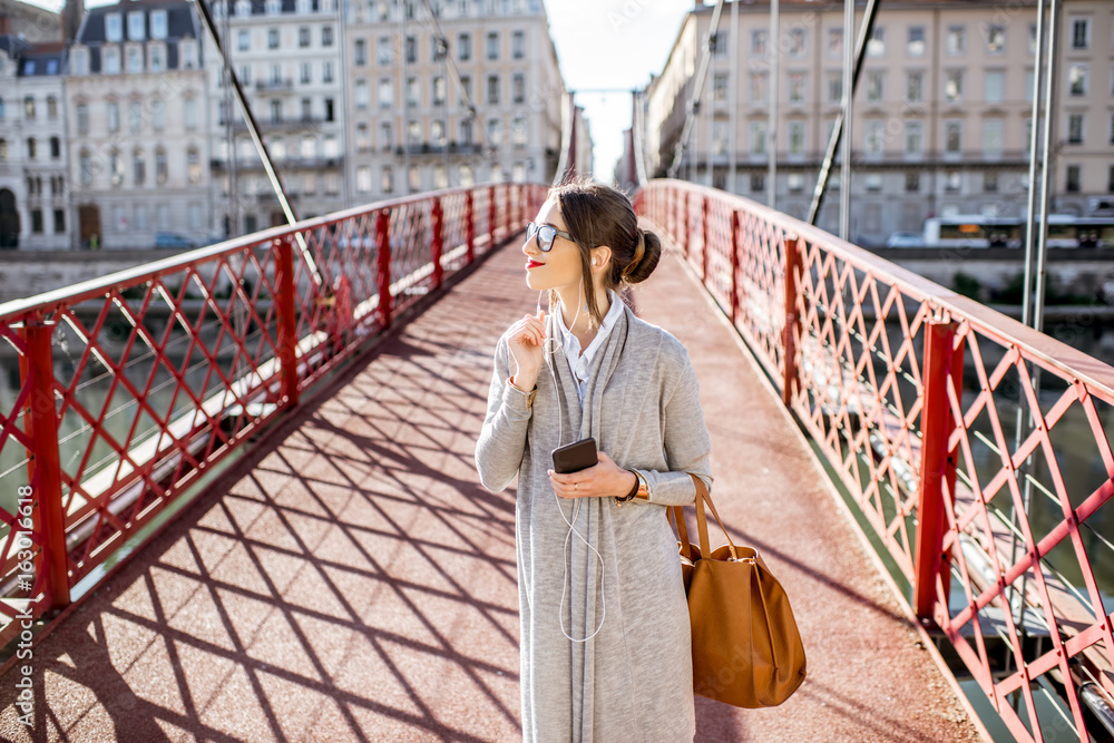 Φωτογραφία Lifestyle portrait of a stylish businesswoman walking on the red bridge in Lyon