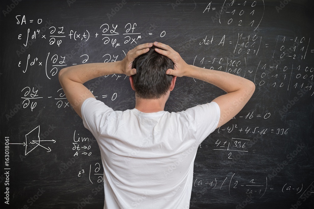 Fotografie Young man is solving mathematical problem on blackboard and is confused