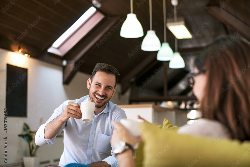 Obraz premium Beautiful young couple drink coffee while sitting on a sofa and looking each other