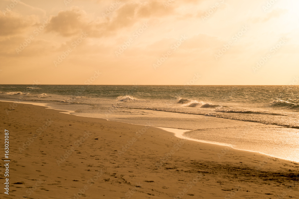 Golden sand of azure calm Caribbean sea shore with waves in summer sunset time