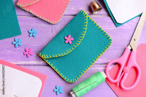 Nice felt purse with flower wooden button. Scissors, thread, needle, thimble, paper templates, flower wooden buttons on a wooden table. Kids hand sewing workshop concept  